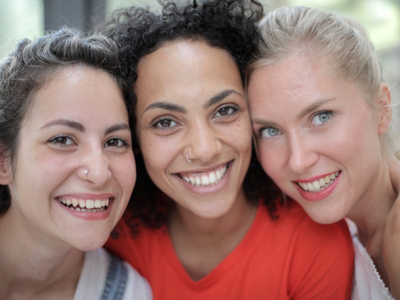 Three women indoors, leaning in close in trust
