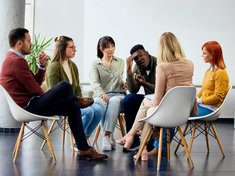 A diverse group seated together, sharing a moment of conversation in a support setting