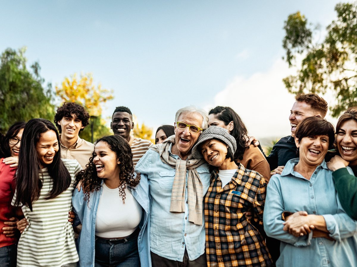 A multigenerational mixed group laughing together at a meal, comfortable and unguarded.